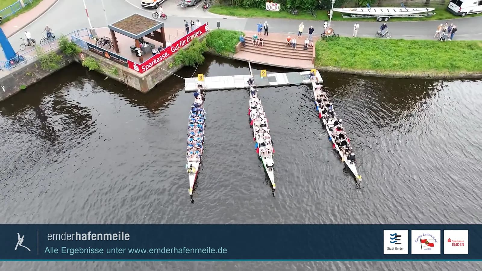 Drei Drachenboote am Start, von oben, mit der Einblendung der Emder Hafenmeile am unteren Rand